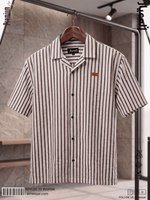 A short-sleeve button-up shirt with vertical dark brown stripes on a cream background, hanging on a wooden hanger from a clothing rack in a store setting.